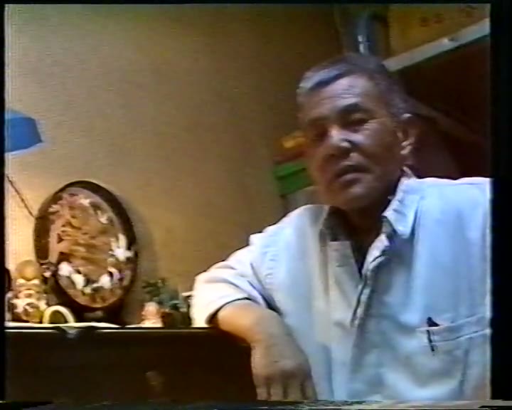 1991年录像中陈松如开口说话的一帧：他一手搭在厨房案台上，面向镜头。